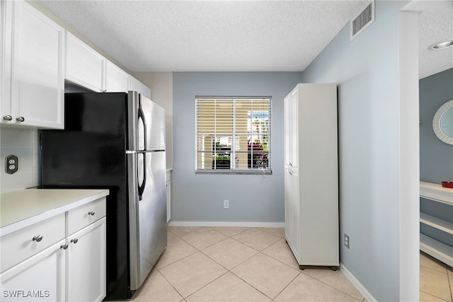 kitchen featuring a textured ceiling, freestanding refrigerator, white cabinetry, light countertops, and light tile patterned flooring