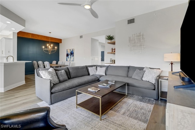 living area featuring visible vents, light wood-style flooring, and ceiling fan with notable chandelier