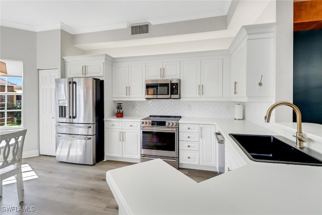 kitchen with white cabinets, a sink, stainless steel appliances, tasteful backsplash, and visible vents