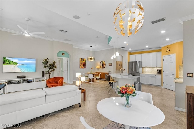 living area featuring ceiling fan with notable chandelier, visible vents, baseboards, ornamental molding, and recessed lighting
