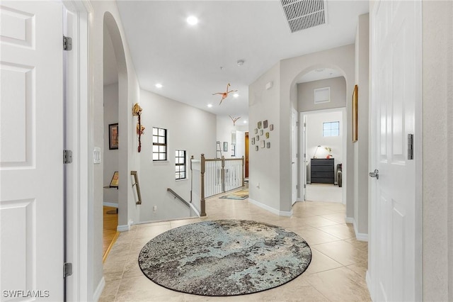 hallway with light tile patterned floors, an upstairs landing, visible vents, baseboards, and arched walkways