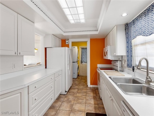 kitchen featuring a tray ceiling, white appliances, a sink, white cabinetry, and washer / dryer