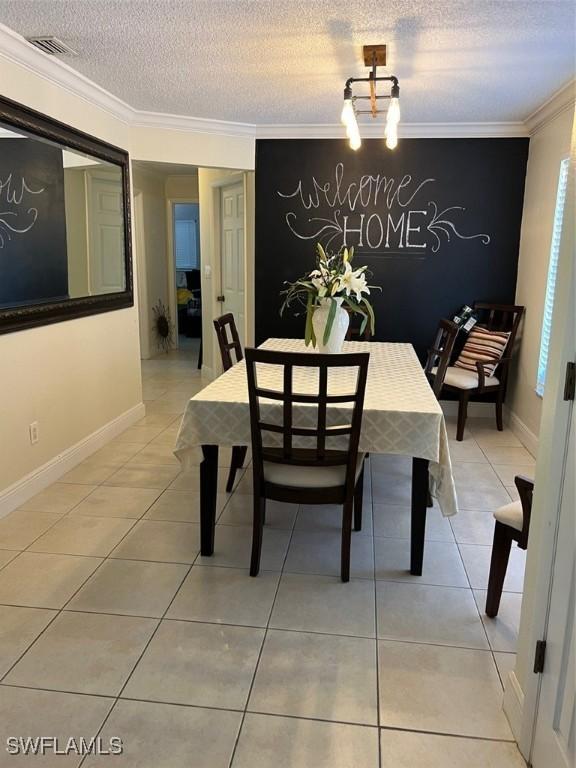 dining space featuring visible vents, crown molding, light tile patterned flooring, baseboards, and a textured ceiling