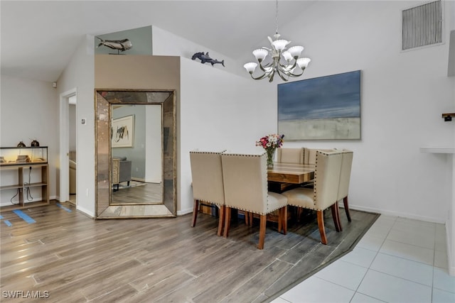 dining room featuring an inviting chandelier, wood finished floors, visible vents, baseboards, and lofted ceiling