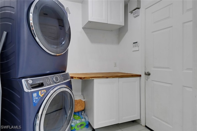 laundry room with stacked washer / dryer, light tile patterned flooring, and cabinet space