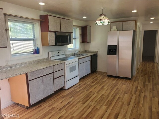 kitchen with a sink, stainless steel appliances, light wood-type flooring, decorative light fixtures, and light countertops