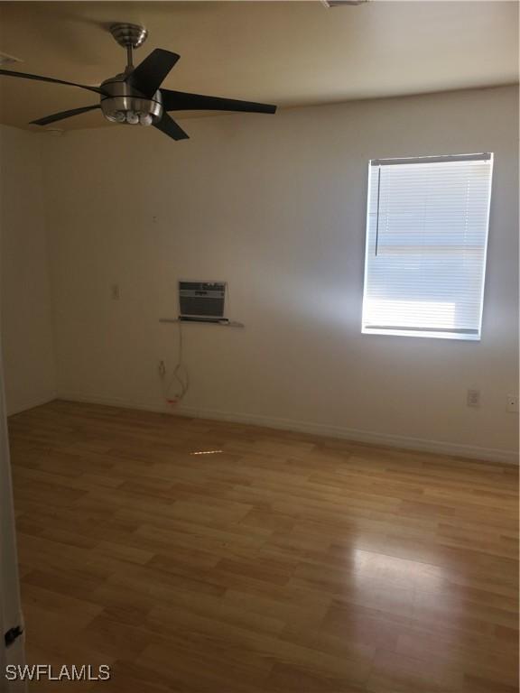 empty room featuring light wood finished floors, a wall mounted AC, baseboards, and a ceiling fan