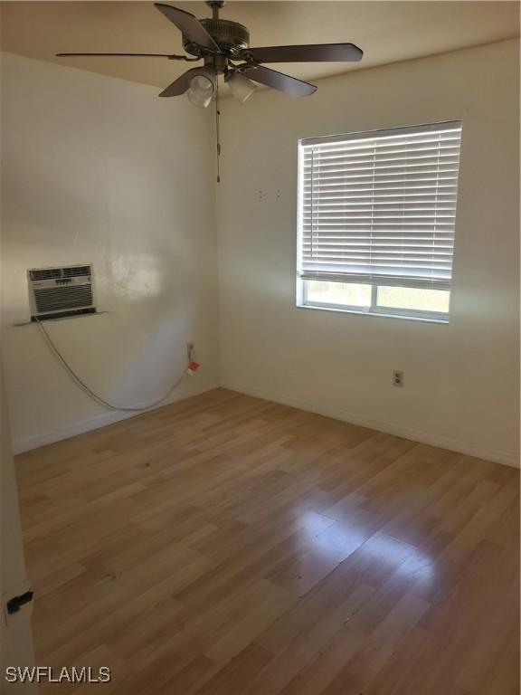 empty room with a wall mounted AC, wood finished floors, baseboards, and ceiling fan