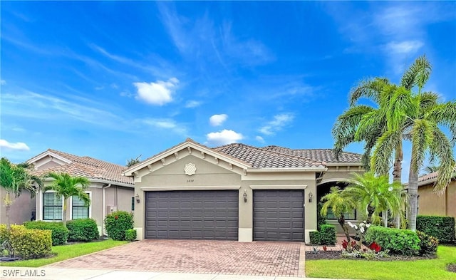view of front of house featuring a garage, a tiled roof, stucco siding, and decorative driveway