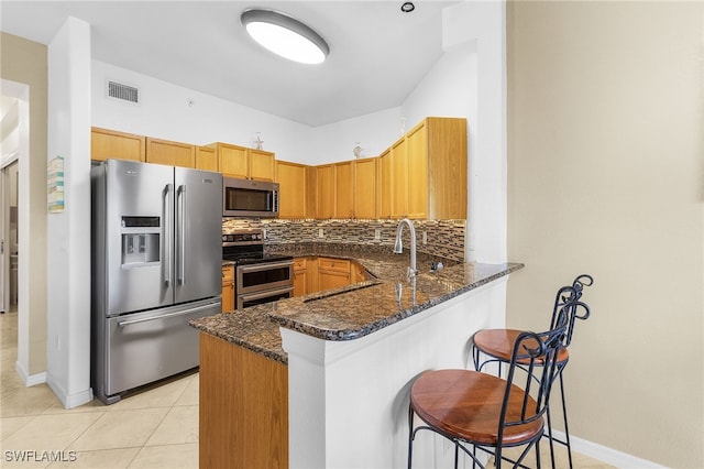 kitchen with a peninsula, stainless steel appliances, dark stone countertops, and visible vents