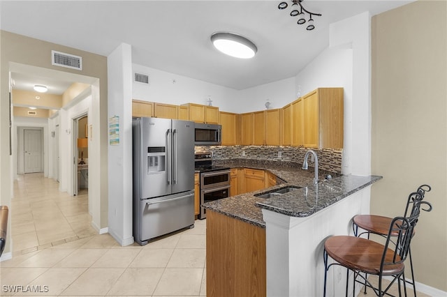 kitchen with a peninsula, dark stone countertops, a sink, stainless steel appliances, and visible vents