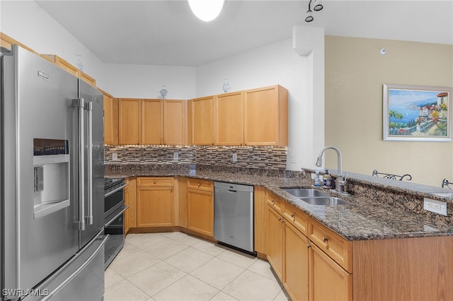kitchen with a sink, a peninsula, backsplash, stainless steel appliances, and dark stone counters