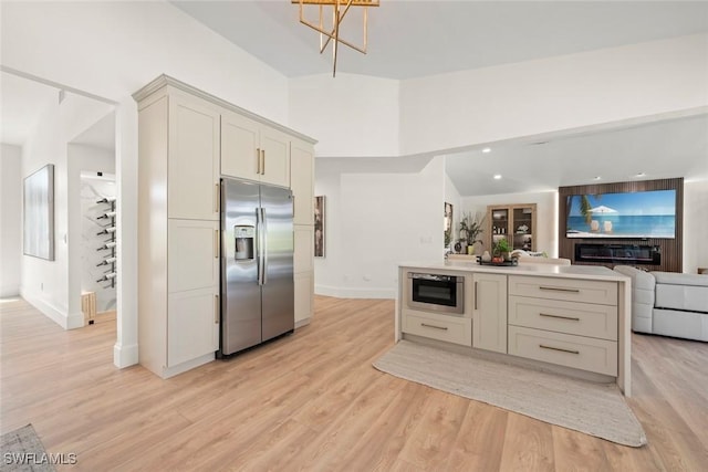 kitchen with stainless steel fridge, light wood-style flooring, open floor plan, baseboards, and light countertops