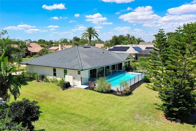 rear view of property with fence, a patio area, an outdoor pool, a tiled roof, and a lawn