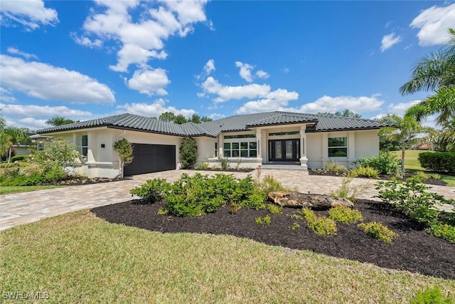 prairie-style home featuring an attached garage, decorative driveway, stucco siding, and french doors