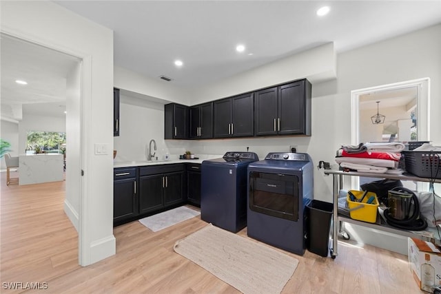 laundry room featuring independent washer and dryer, light wood-type flooring, a sink, and cabinet space
