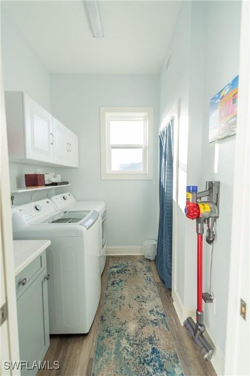 clothes washing area featuring washer and clothes dryer, cabinet space, light wood-type flooring, and baseboards