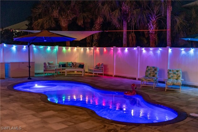 pool at night with a patio area, an outdoor living space, a hot tub, and fence