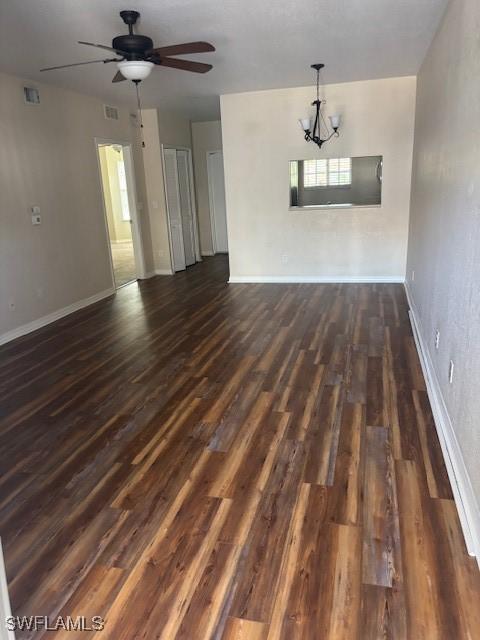 unfurnished dining area featuring dark wood-style flooring, a chandelier, ceiling fan, and baseboards