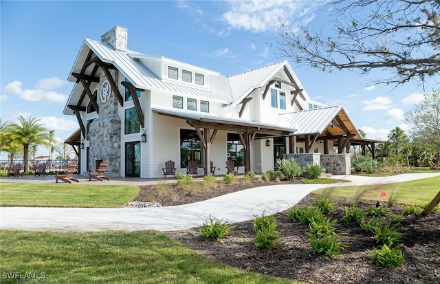 modern farmhouse style home with stone siding, a front yard, metal roof, a chimney, and a standing seam roof
