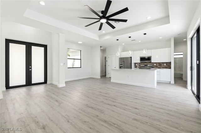 unfurnished living room featuring ceiling fan, light wood-style floors, a tray ceiling, and recessed lighting