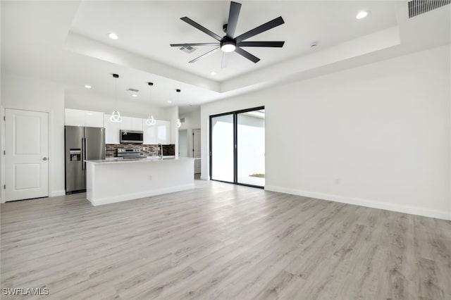 unfurnished living room with a tray ceiling, light wood finished floors, visible vents, and recessed lighting