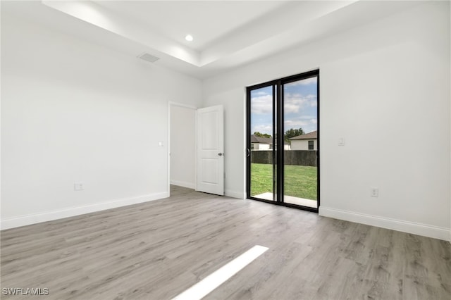 spare room with light wood finished floors, a raised ceiling, and baseboards