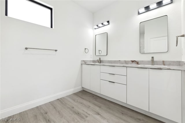 full bath featuring double vanity, wood finished floors, baseboards, and a sink