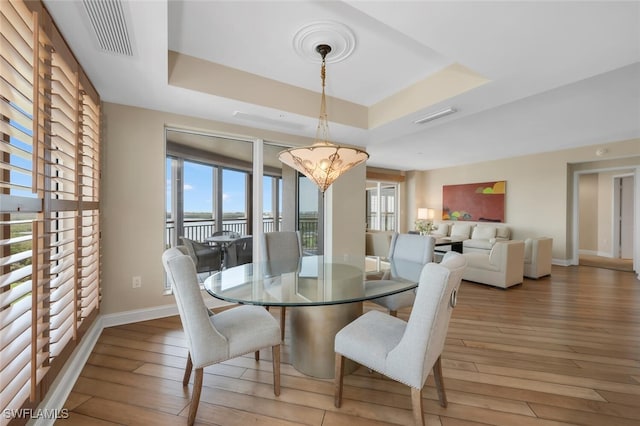 dining area featuring baseboards, visible vents, a water view, a raised ceiling, and light wood-style floors