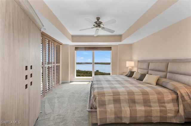 bedroom with carpet flooring, a water view, a ceiling fan, and a tray ceiling
