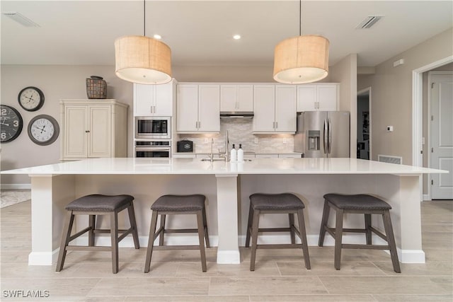 kitchen featuring appliances with stainless steel finishes, baseboards, a sink, backsplash, and a large island with sink
