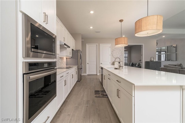 kitchen with a sink, stainless steel appliances, under cabinet range hood, white cabinetry, and light countertops