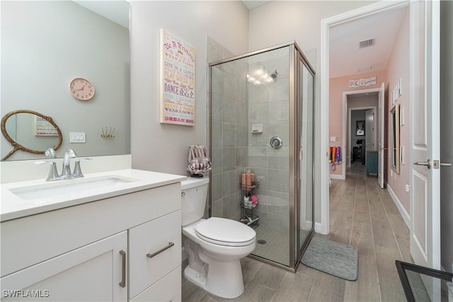 bathroom featuring toilet, wood finished floors, a stall shower, visible vents, and vanity