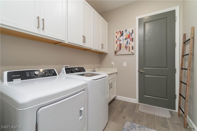 clothes washing area featuring baseboards, a sink, wood finish floors, washer and clothes dryer, and cabinet space