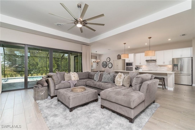 living area featuring a tray ceiling, visible vents, ceiling fan with notable chandelier, and recessed lighting