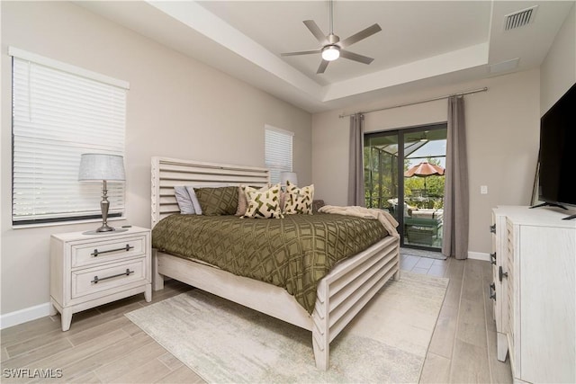 bedroom with light wood finished floors, access to outside, baseboards, and a raised ceiling