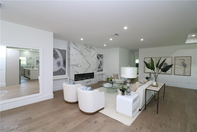 living room featuring recessed lighting, baseboards, visible vents, a high end fireplace, and wood finished floors