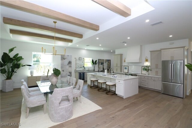 dining area featuring light wood-type flooring, wine cooler, beamed ceiling, and recessed lighting