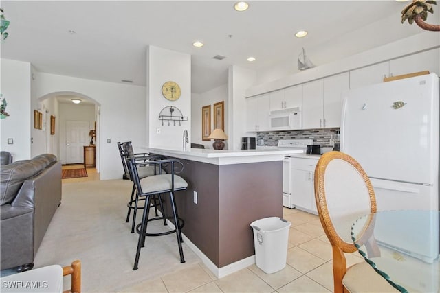 kitchen featuring white appliances, arched walkways, a breakfast bar, a peninsula, and white cabinets