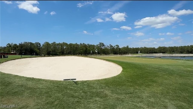 view of property's community with a water view, an area to practice putting, a lawn, and view of wooded area