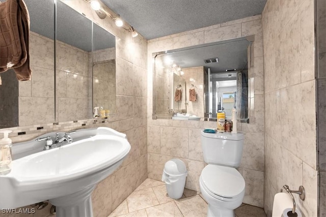 bathroom with tile walls, toilet, tile patterned floors, a textured ceiling, and a sink