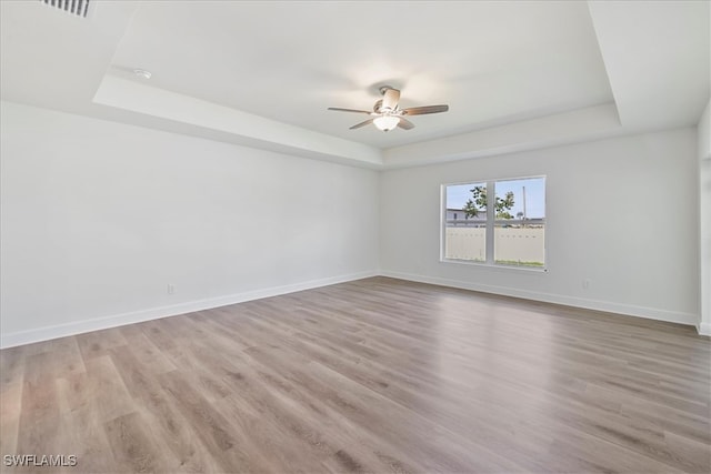 unfurnished room featuring a tray ceiling, a ceiling fan, and wood finished floors