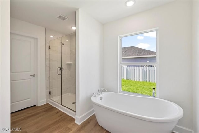 bathroom featuring a stall shower, baseboards, visible vents, a soaking tub, and wood finished floors