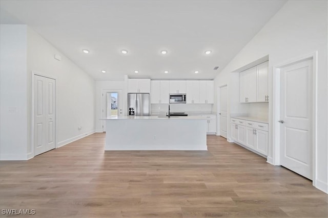 kitchen with a center island with sink, white cabinetry, light countertops, appliances with stainless steel finishes, and lofted ceiling