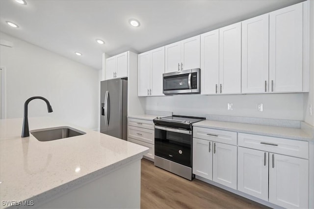 kitchen with wood finished floors, a sink, stainless steel appliances, white cabinets, and recessed lighting