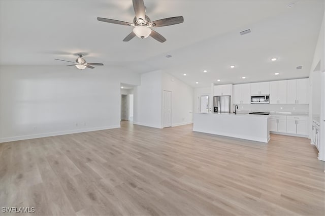 unfurnished living room featuring lofted ceiling, light wood-style floors, ceiling fan, and a sink