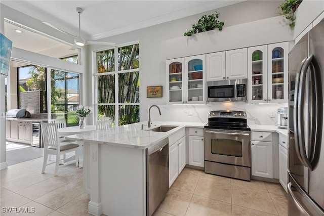 kitchen featuring stainless steel appliances, a sink, a peninsula, wine cooler, and tasteful backsplash