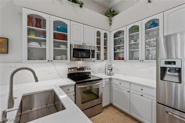 kitchen with appliances with stainless steel finishes, a sink, ornamental molding, light stone counters, and backsplash