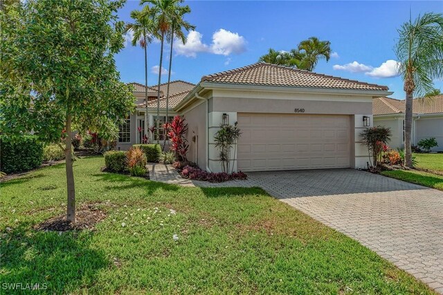 view of front of property with stucco siding, an attached garage, a tile roof, decorative driveway, and a front lawn