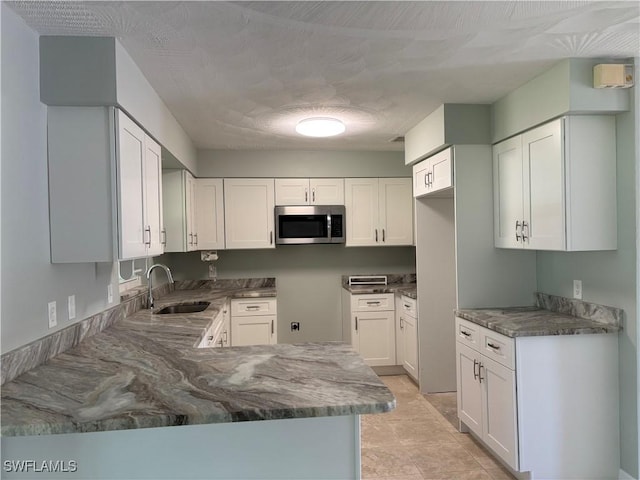 kitchen featuring stone counters, white cabinetry, stainless steel microwave, and a sink